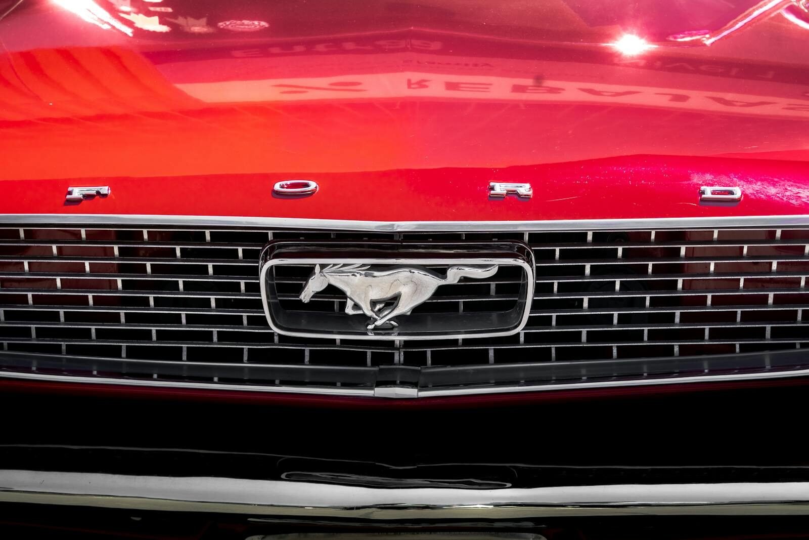 Detailed close-up of the iconic grille of a vintage red Ford Mustang.