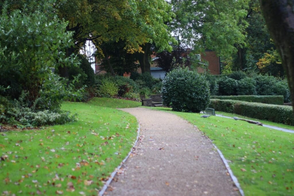 Tranquil garden path surrounded by lush greenery and trees in a serene park.