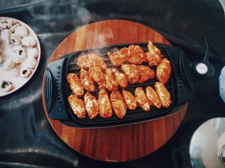 Top view of delicious spicy chicken wings grilling on an electric grill with mushrooms nearby.