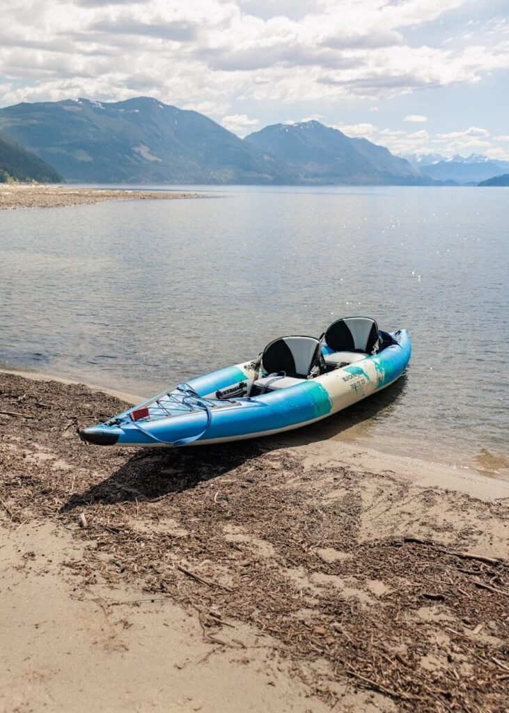 Kayak on sandy shore by a lake with mountains.