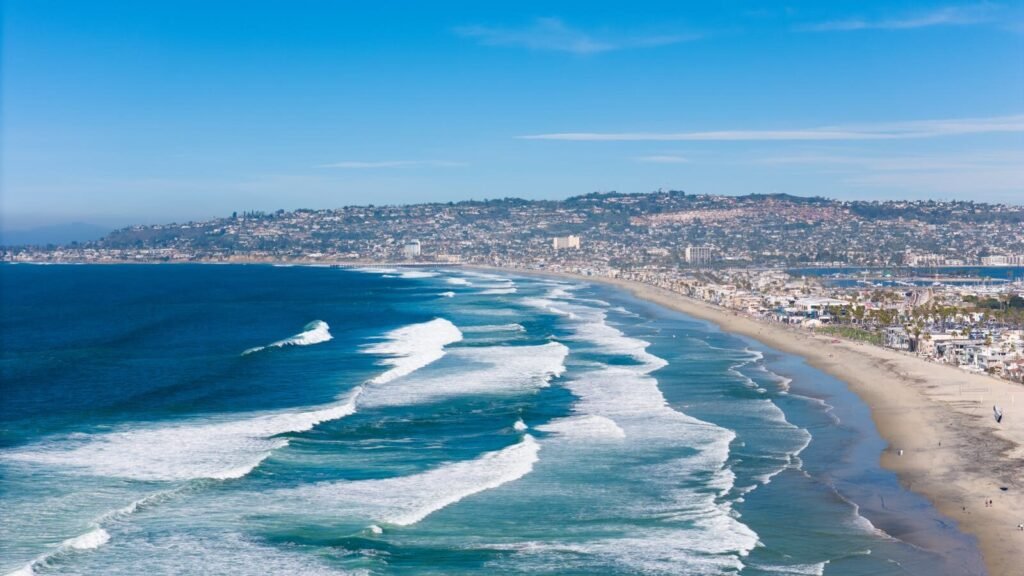A breathtaking aerial shot of San Diego's coastline, capturing waves and cityscape under a clear sky.