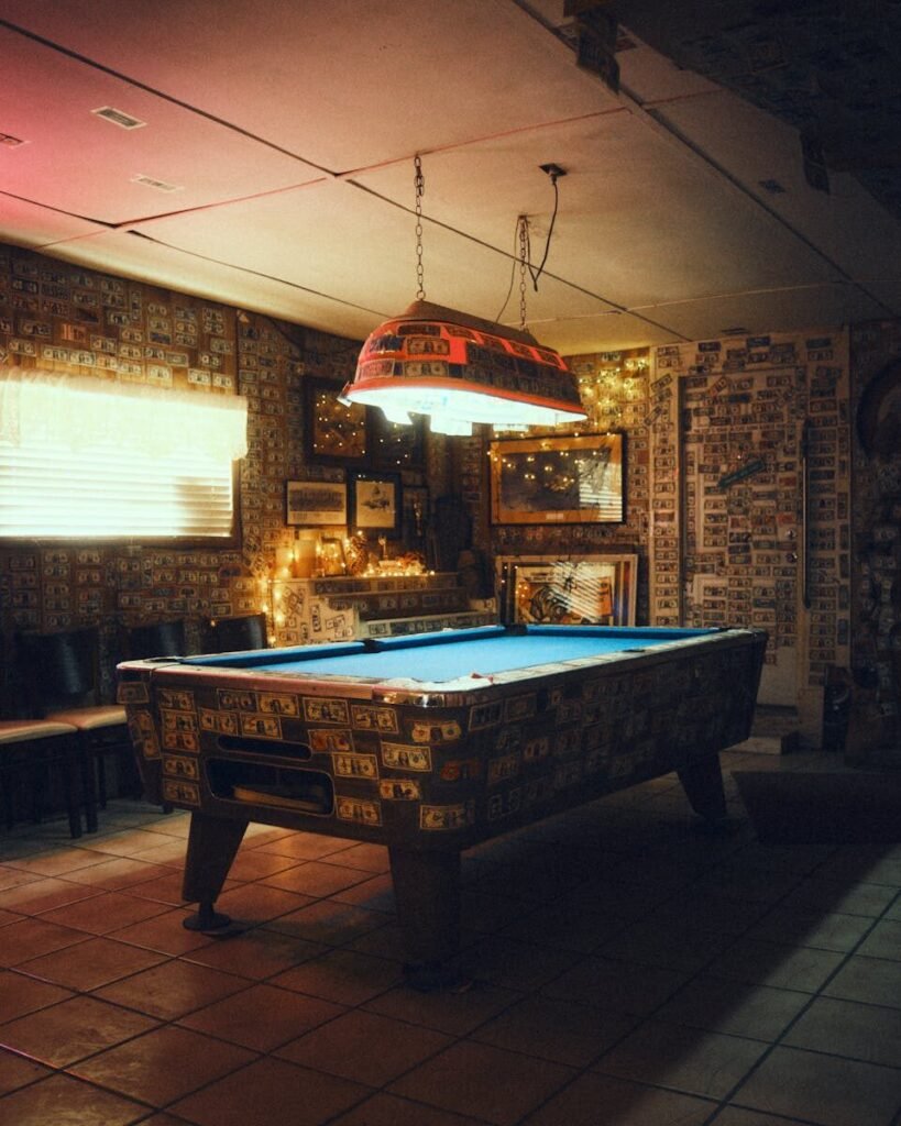 man cave essentials ; Cozy interior with a pool table and decorative lighting in Bombay Beach, California.