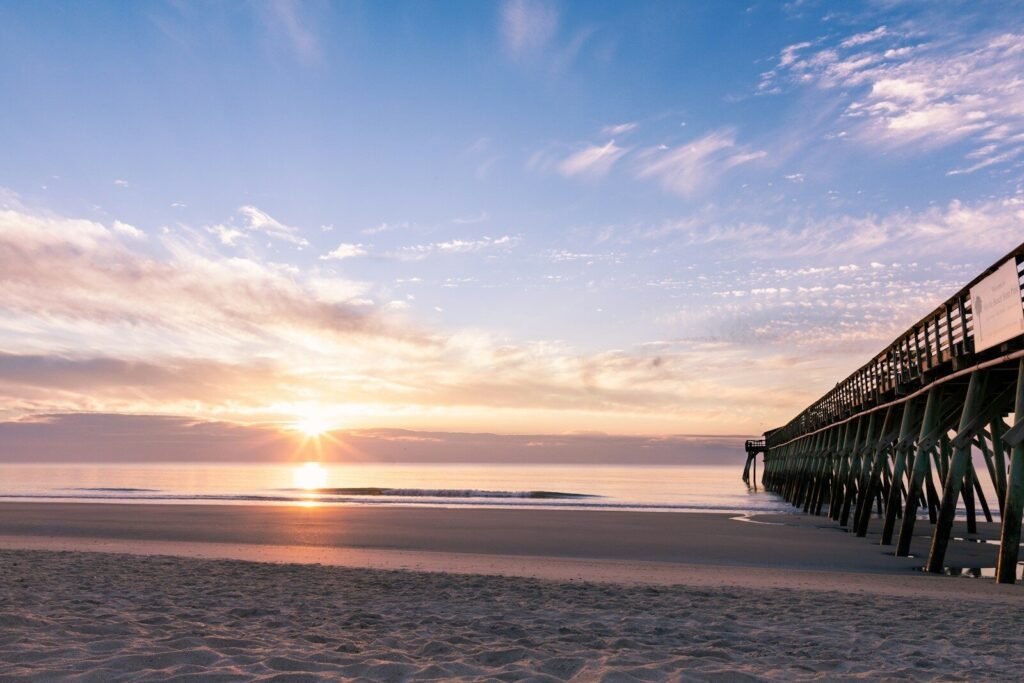 Top U.S. Beaches; silhouette photography of black wooden dock near shoreline during sunrise