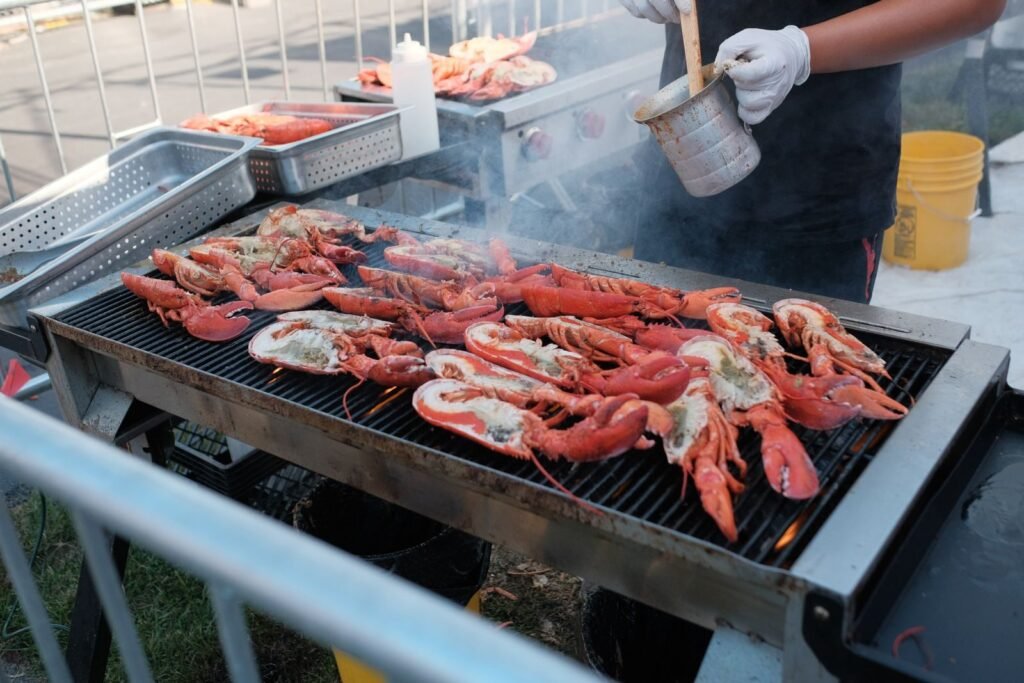 Fresh lobsters being grilled outdoors on a barbecue with seasoning for a flavorful meal.