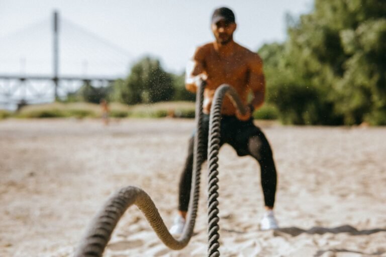 Outdoor Fitness Trends; Man exercising with battle ropes on a sunny beach, showcasing strength and determination.