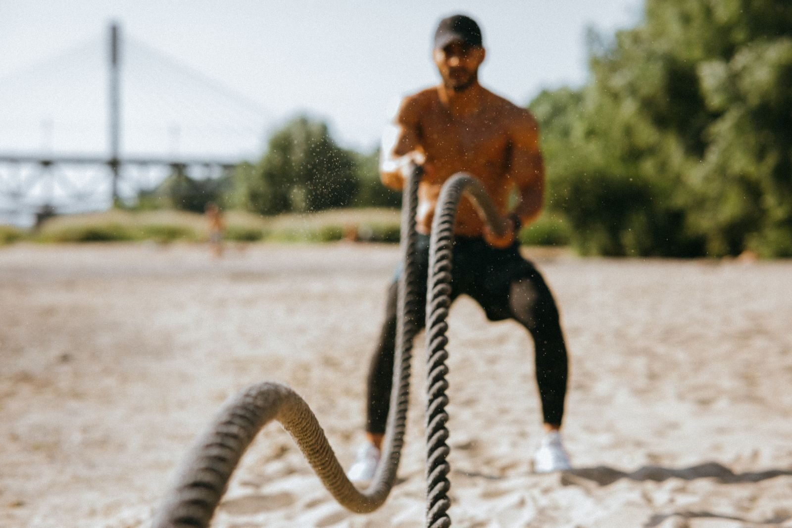 Outdoor Fitness Trends; Man exercising with battle ropes on a sunny beach, showcasing strength and determination.
