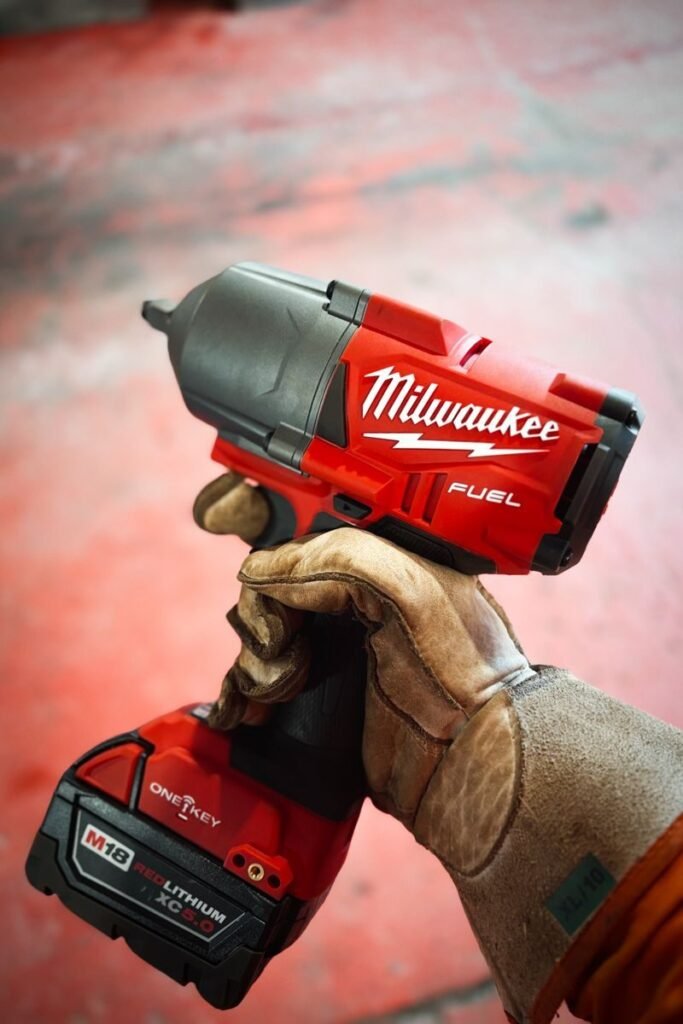 Milwaukee vs. DeWalt; A gloved hand holding a red and black power tool with a blurred background.