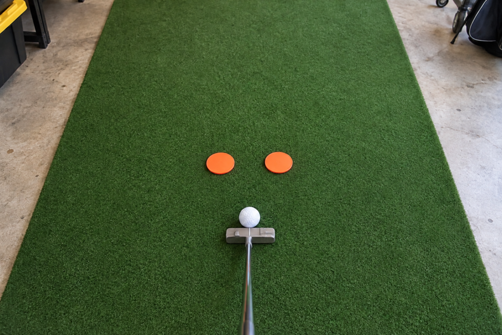 Golf ball and putter behind two orange markers forming a putting gate.